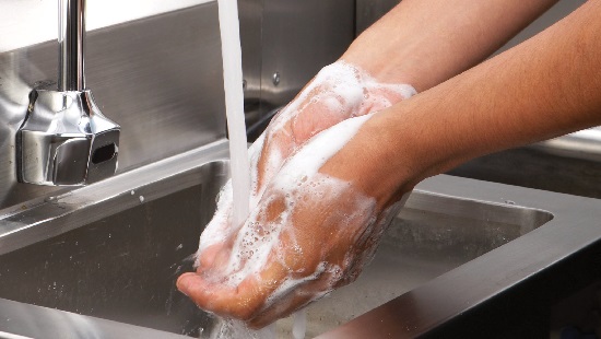 Washing hands with soap in industrial sink.