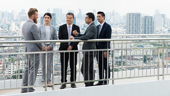 Business professionals standing on bridge outside participating in meeting.