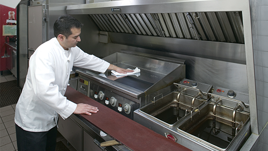 清洁烤架的厨师 Chef cleaning a stainless-steel grill from grease residue in a commercial kitchen.