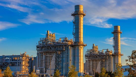 Massive gas fired power plant near a long mountain range on a sunny day.
