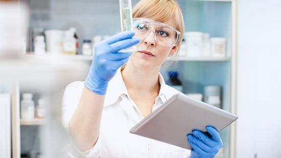 Scientist Looking at Measuring Cylinder, Holding a Tablet