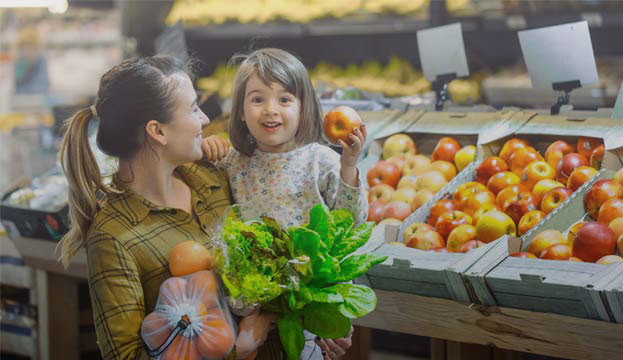 Mother holding smiling child next to fruit stand